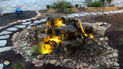 Illuminated garden water feature with rocks and lights.