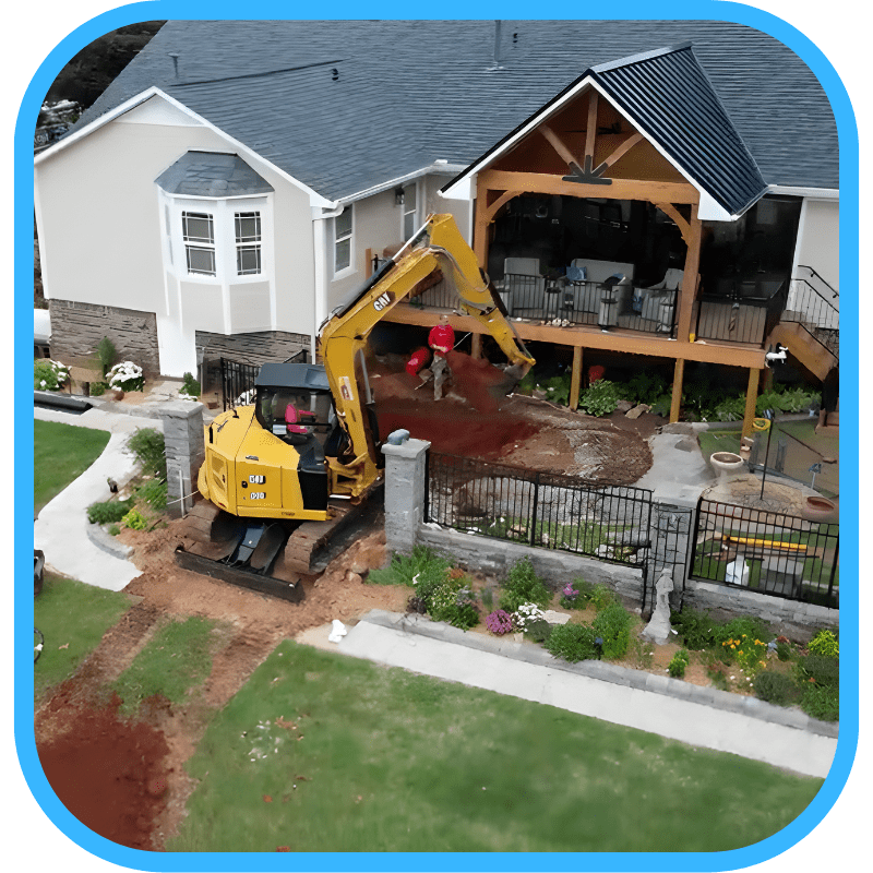 Yellow excavator working near house with patio during pond construction