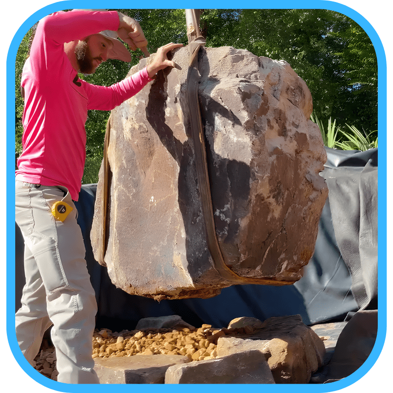 MDA team member lifting large boulder with strap during construction